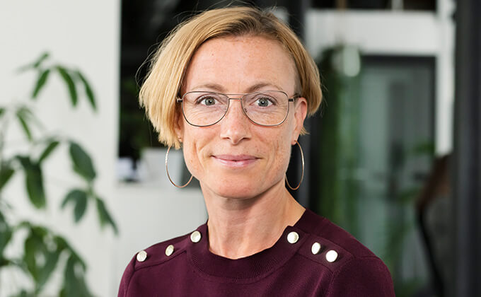  Image for En kvinna med blont hår och glasögon som tittar in i kameran med ett leende