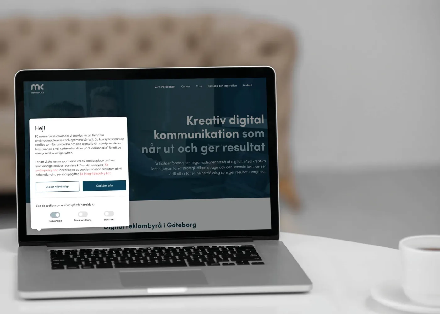 En bärbar dator på ett vitt bord visar en webbplats med ett popup-fönster för samtycke till kakor.